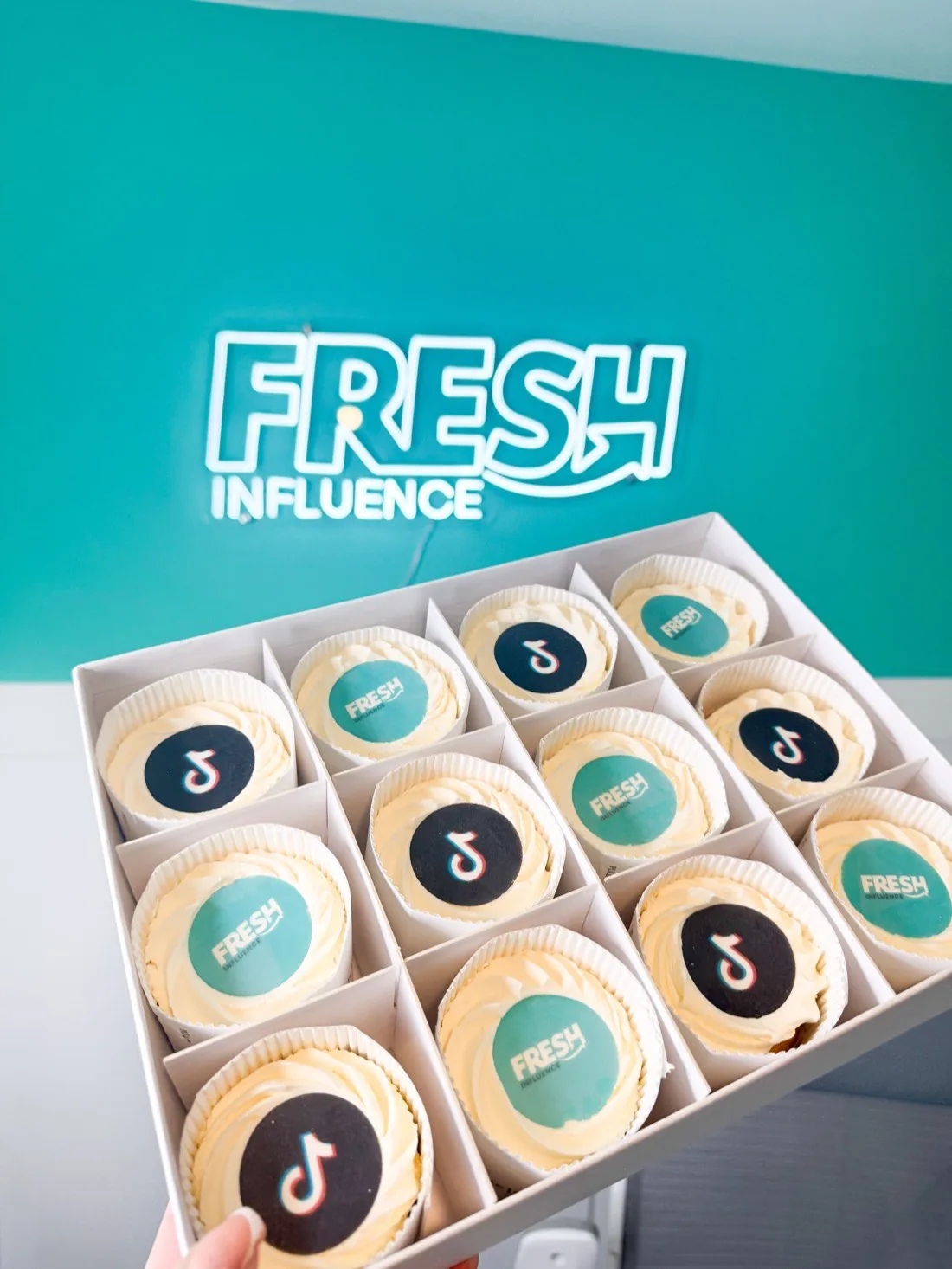 Fresh Influence branded cupcakes in front of the studio neon sign